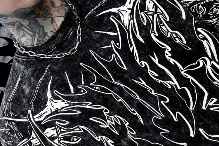 Detailed close-up of a black acid-wash t-shirt with bold white flame-like graphics, highlighting the print near the neckline and shoulder.