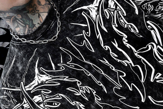 Detailed close-up of a black acid-wash t-shirt with bold white flame-like graphics, highlighting the print near the neckline and shoulder.