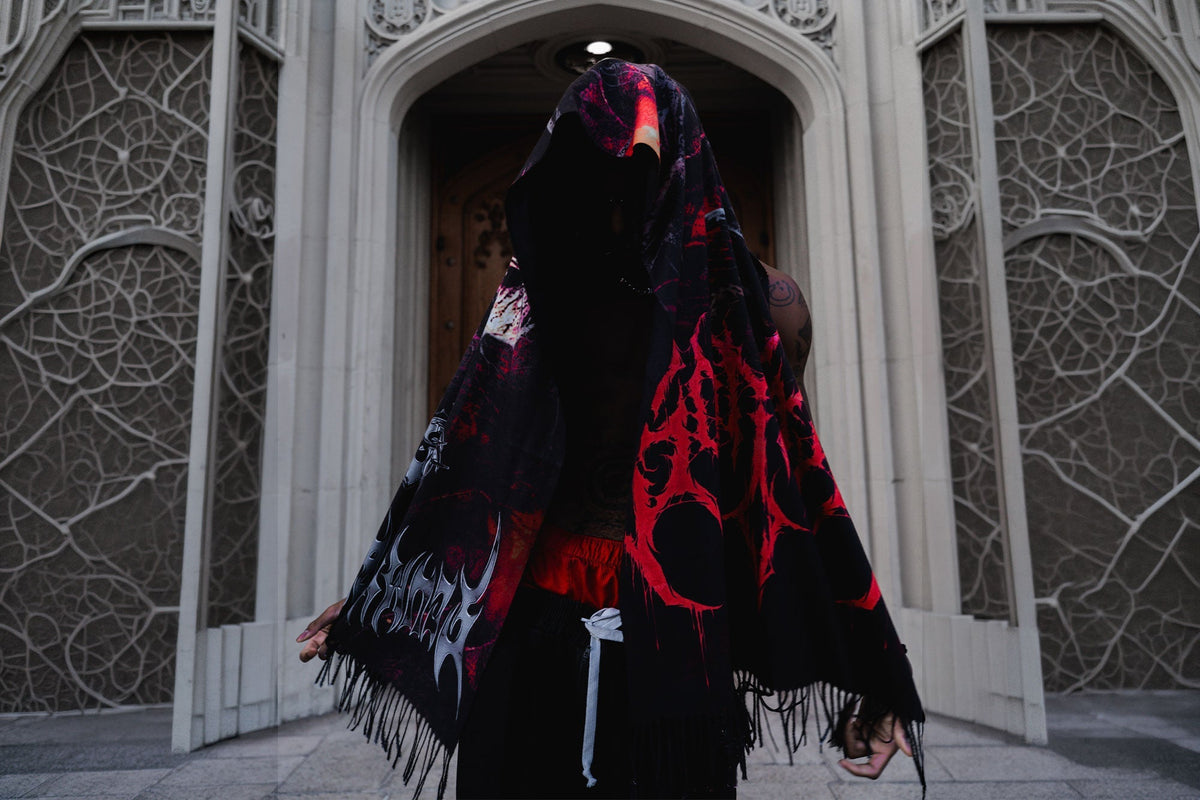Person wearing a red and black Scummy Bears pashmina over their head and shoulders in front of an ornate stone doorway